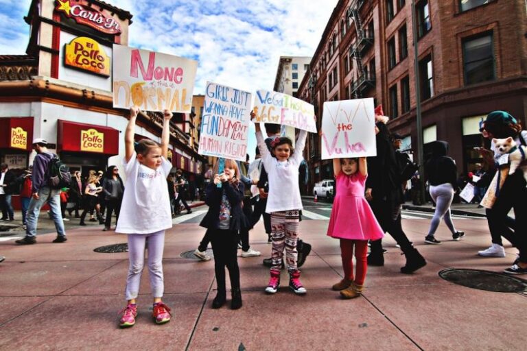 Hamster Signs - four children raising up a banner at the middle of a busy street during day time